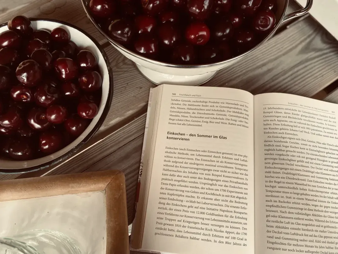 Ein aufgeschlagenes Buch zum Einkochen liegt neben zwei Schalen mit dunklen Kirschen.